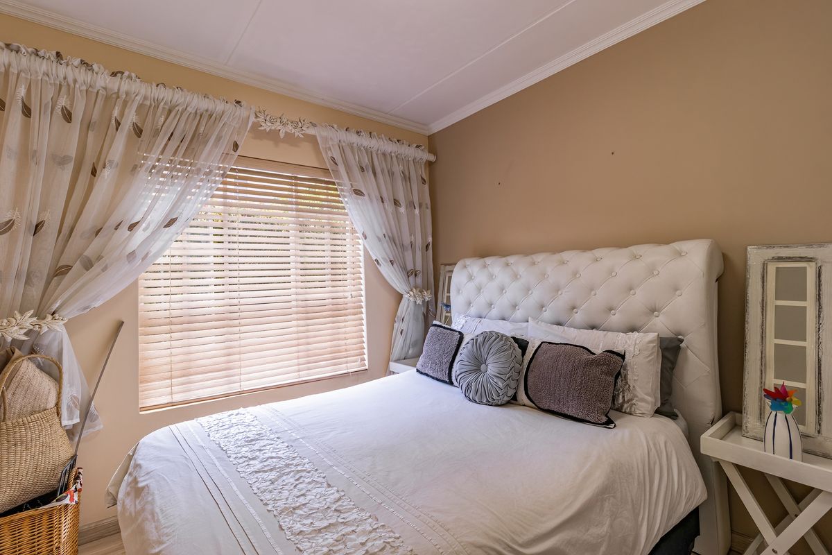 A cozy bedroom featuring neutral wall tones, crown molding, and venetian blinds providing natural light control.