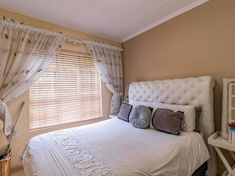 A cozy bedroom featuring neutral wall tones, crown molding, and venetian blinds providing natural light control.