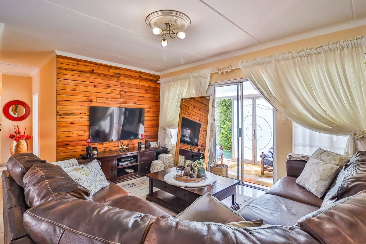 A cozy living room featuring a wood-paneled accent wall, tiled flooring, and sliding glass doors that provide direct access to the outdoor patio area.