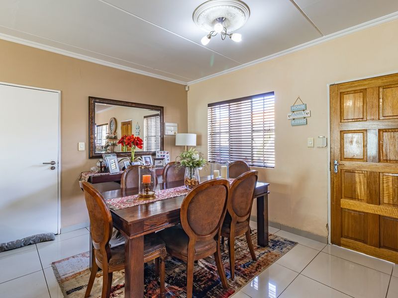 A dining room featuring tiled flooring, a ceiling rose, and natural light through venetian blinds, providing a functional space for family meals.