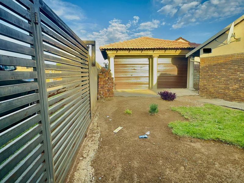 Front exterior view featuring a double garage with roll-up doors, a metal sliding gate, and a face brick facade with a small garden area.
