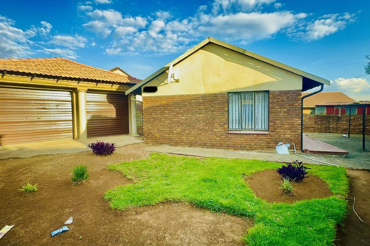 Rear view of the property featuring a brick facade, tiled roof, double garage with roller shutter doors, and a small garden area.