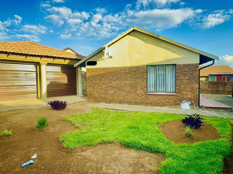 Rear view of the property featuring a brick facade, tiled roof, double garage with roller shutter doors, and a small garden area.