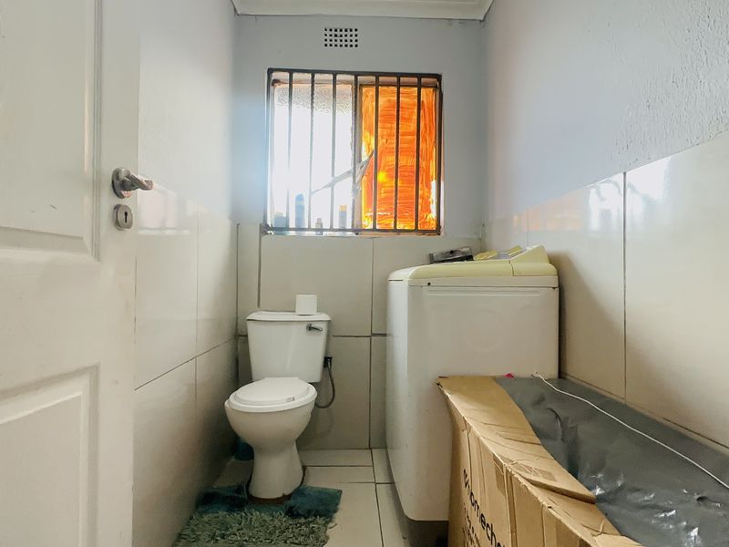 A functional laundry room featuring tiled walls and flooring, equipped with a toilet and plumbing connections for a washing machine.