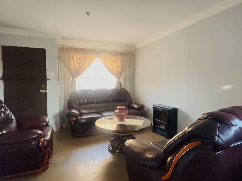 A living room featuring neutral walls, coving, and standard window treatments, currently showing signs of wear on the flooring and wall surfaces.