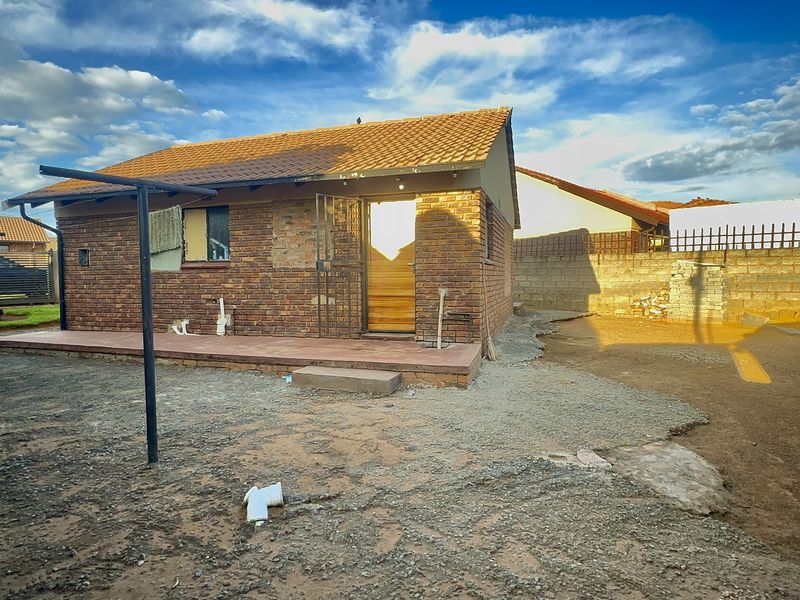 Rear view of a brick house featuring a tiled roof, a concrete patio area, and an enclosed yard with perimeter walling.
