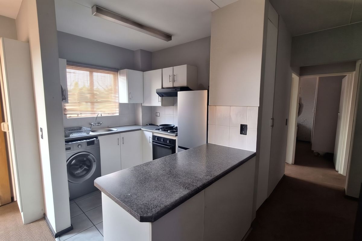 Compact kitchen featuring white cabinetry, laminate countertops, a breakfast bar, and integrated appliances, offering a functional layout for an apartment setting.