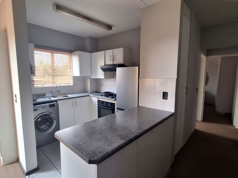 Compact kitchen featuring white cabinetry, laminate countertops, a breakfast bar, and integrated appliances, offering a functional layout for an apartment setting.