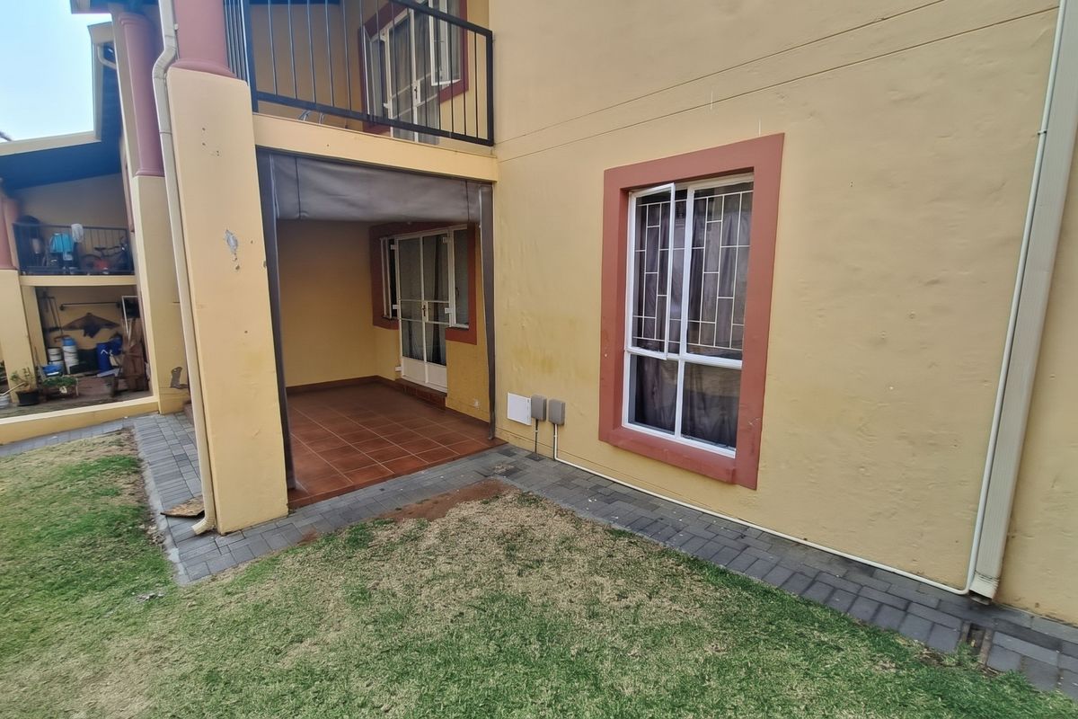 Rear view of the apartment featuring a covered tiled patio, a small private garden area, and an upper-level balcony with security bars.