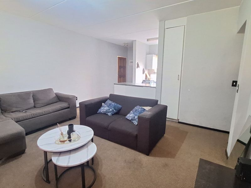 Open plan living area featuring carpeted flooring, a built-in storage cupboard, and a partial view into the adjacent kitchen space.