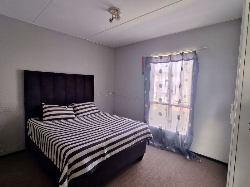 A bedroom featuring carpeted flooring and a window with security bars, currently showing significant signs of wall moisture damage and peeling paint.