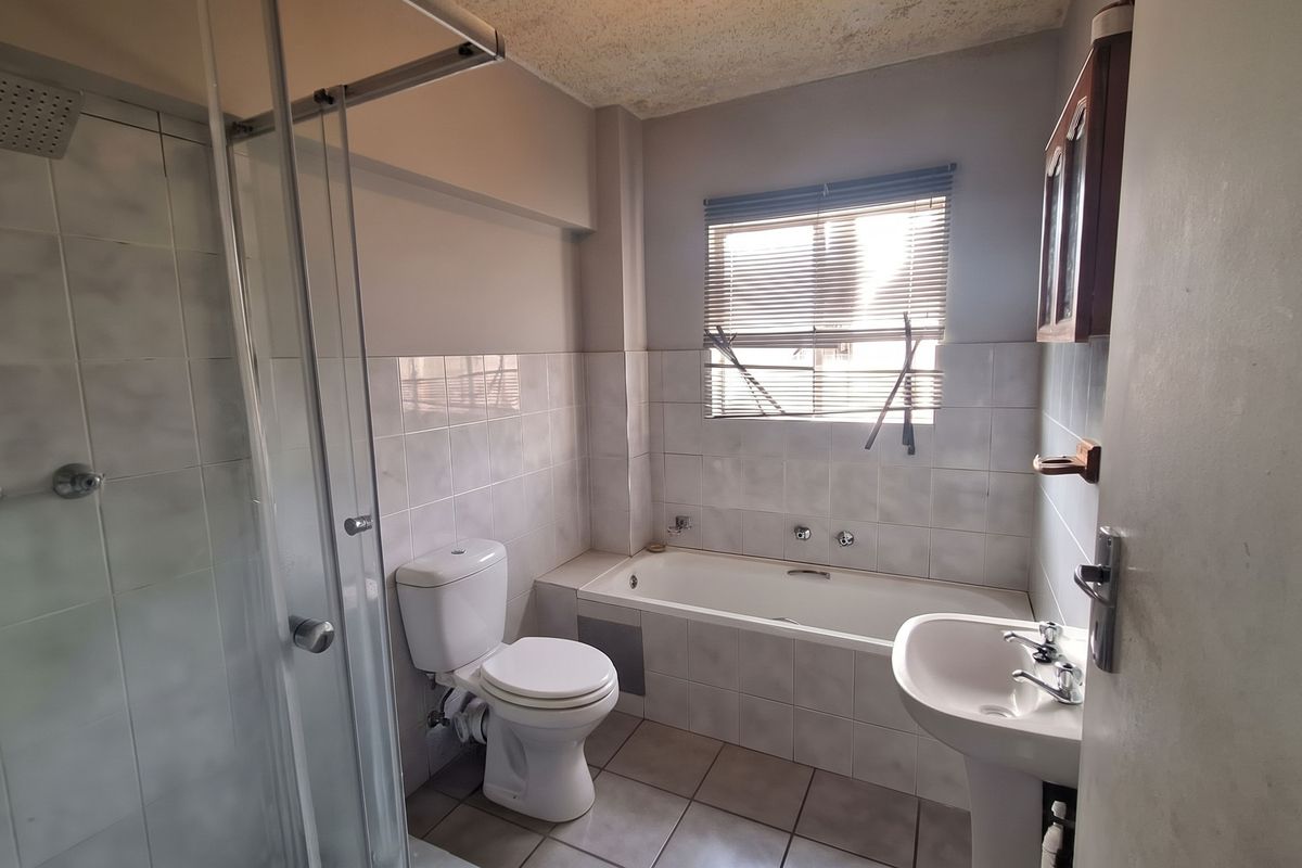 A dated bathroom featuring a shower enclosure, bathtub, pedestal basin, and toilet, with tiled finishes throughout. The space requires cosmetic updates.