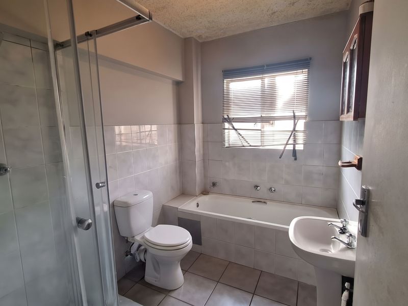A dated bathroom featuring a shower enclosure, bathtub, pedestal basin, and toilet, with tiled finishes throughout. The space requires cosmetic updates.