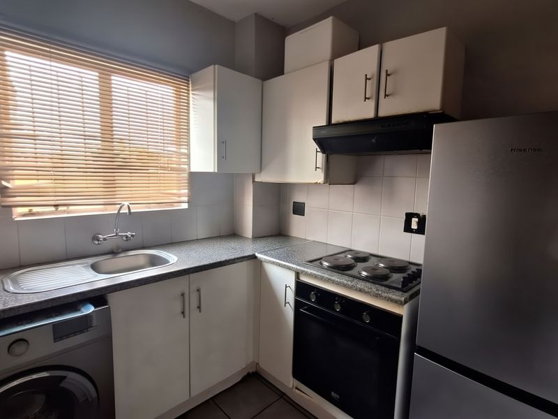A functional kitchen featuring built-in cabinetry, a stainless steel sink, electric hob, oven, and extractor fan with tiled splashbacks.