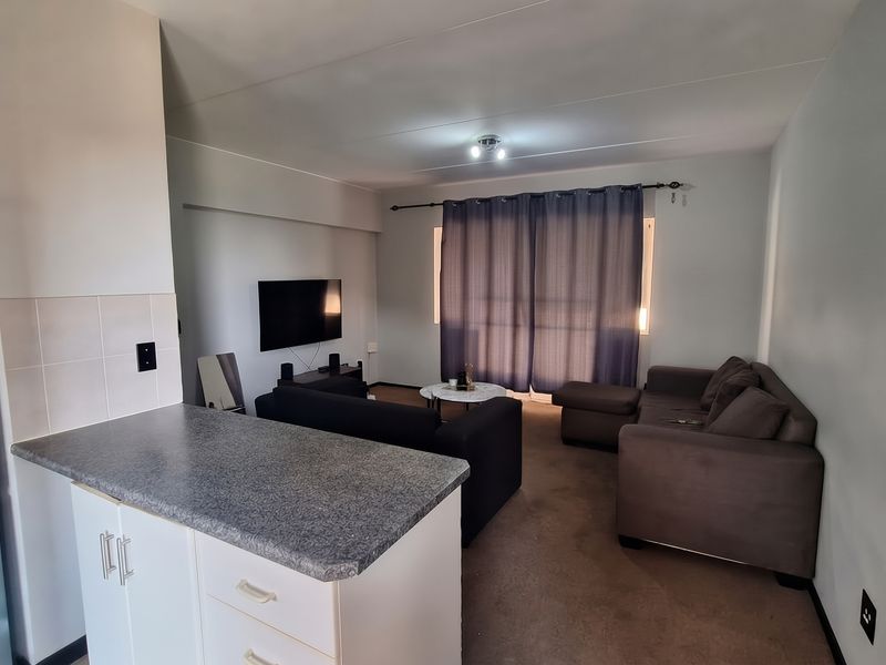 An open-plan living area featuring a kitchen with a breakfast counter and a connected lounge space with neutral finishes.