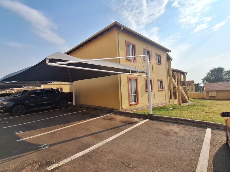 Exterior view of an apartment complex featuring designated asphalt parking bays with shade cloth carports and an external staircase.