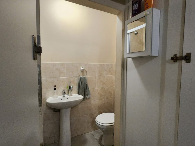A compact bathroom featuring a pedestal basin, toilet, and tiled finishes, providing essential functionality in a modest space.
