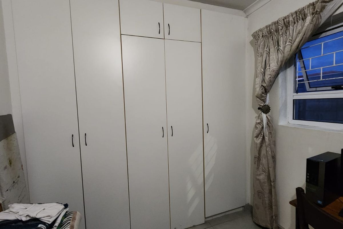A bedroom featuring floor-to-ceiling built-in cupboards and a window fitted with security bars.
