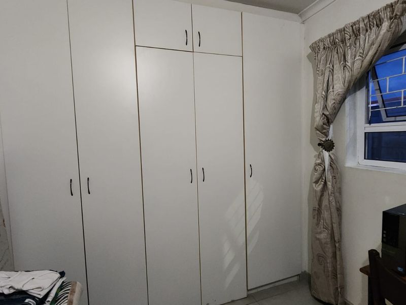 A bedroom featuring floor-to-ceiling built-in cupboards and a window fitted with security bars.