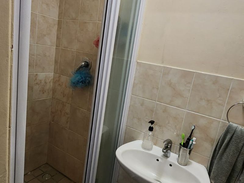 A functional bathroom featuring a pedestal basin and a glass-enclosed shower with tiled finishes.