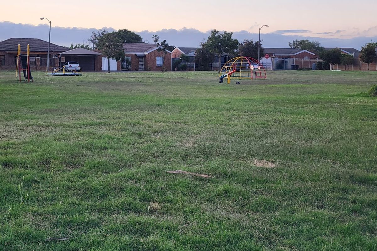 A view of a communal grassed area and playground equipment located behind the residential townhouse properties.