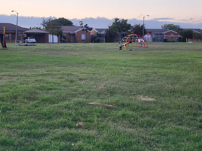 A view of a communal grassed area and playground equipment located behind the residential townhouse properties.
