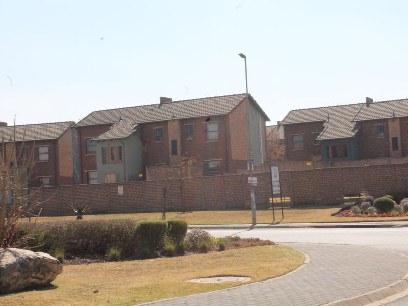 A street-level view of a residential apartment complex featuring brick facades, tiled roofs, and a secure perimeter wall.
