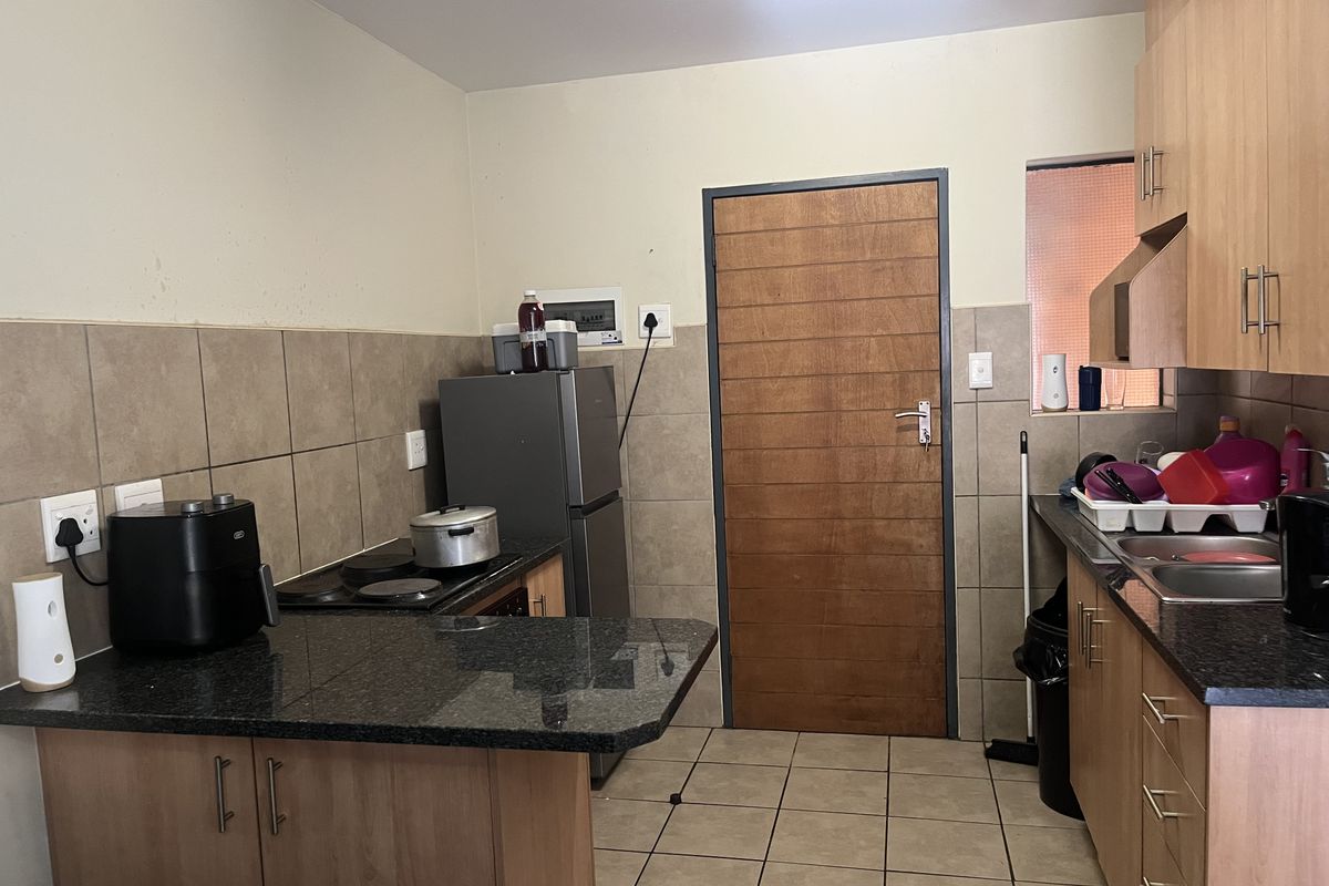 Functional kitchen featuring wooden cabinetry, granite countertops, a built-in hob, and tiled finishes throughout.