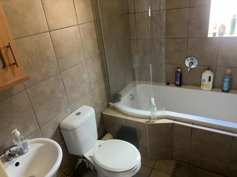 A functional bathroom featuring a bathtub with a glass shower screen, a pedestal basin, and a toilet, finished with neutral wall tiling.