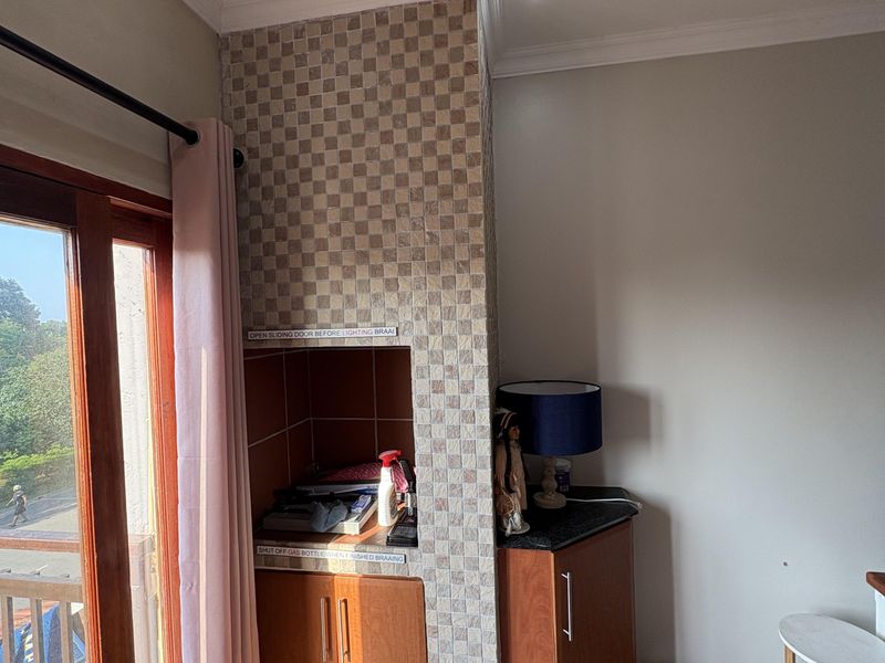 A covered balcony area featuring a built-in braai with tiled surround, wooden cabinetry, and direct access to the outdoors via a sliding door.