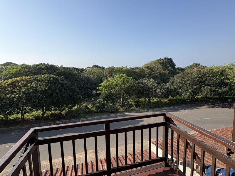 An elevated wooden balcony featuring a timber balustrade, offering an open view of the surrounding trees and street.