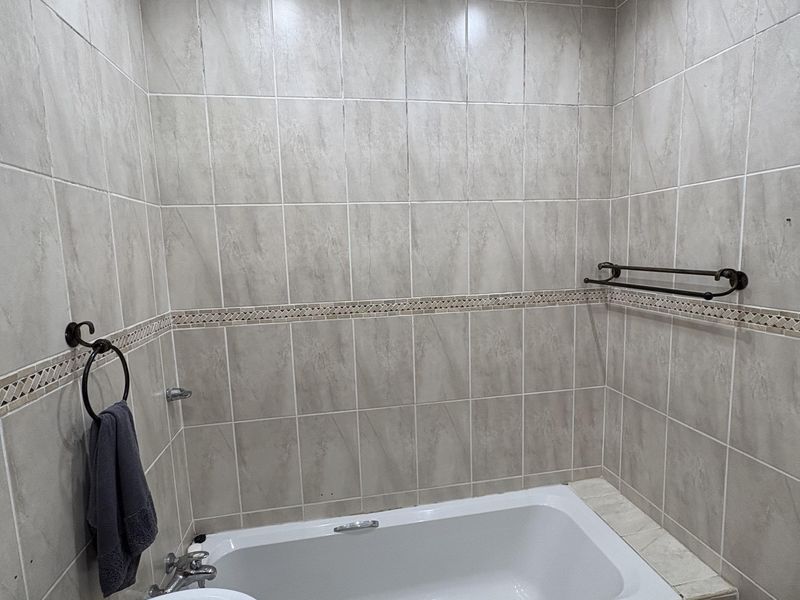 A clean and functional bathroom featuring a built-in bathtub, vanity basin, and neutral wall tiling with decorative border accents.