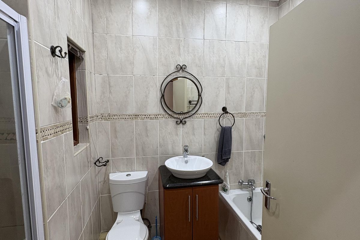 A functional bathroom featuring a vanity with a vessel sink, a standard toilet, and a bathtub with full-height wall tiling.