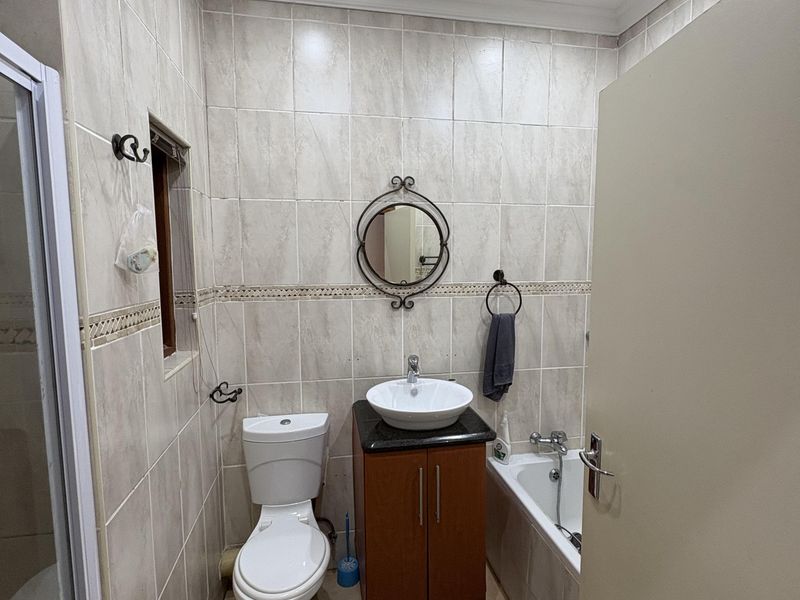A functional bathroom featuring a vanity with a vessel sink, a standard toilet, and a bathtub with full-height wall tiling.