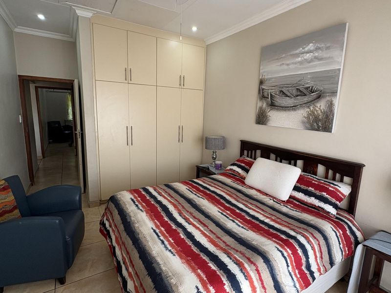 A functional bedroom featuring built-in cupboards, a ceiling fan, and tiled flooring, offering a neutral base for potential interior updates.
