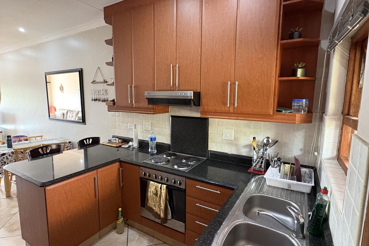 A functional kitchen featuring wooden cabinetry, granite countertops, a stainless steel double sink, and built-in cooking appliances with tiled flooring and backsplash.