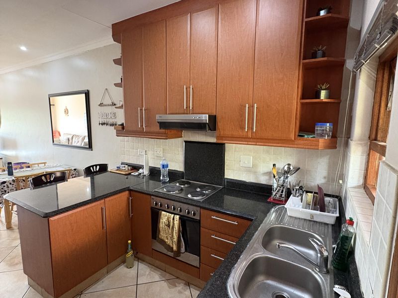 A functional kitchen featuring wooden cabinetry, granite countertops, a stainless steel double sink, and built-in cooking appliances with tiled flooring and backsplash.