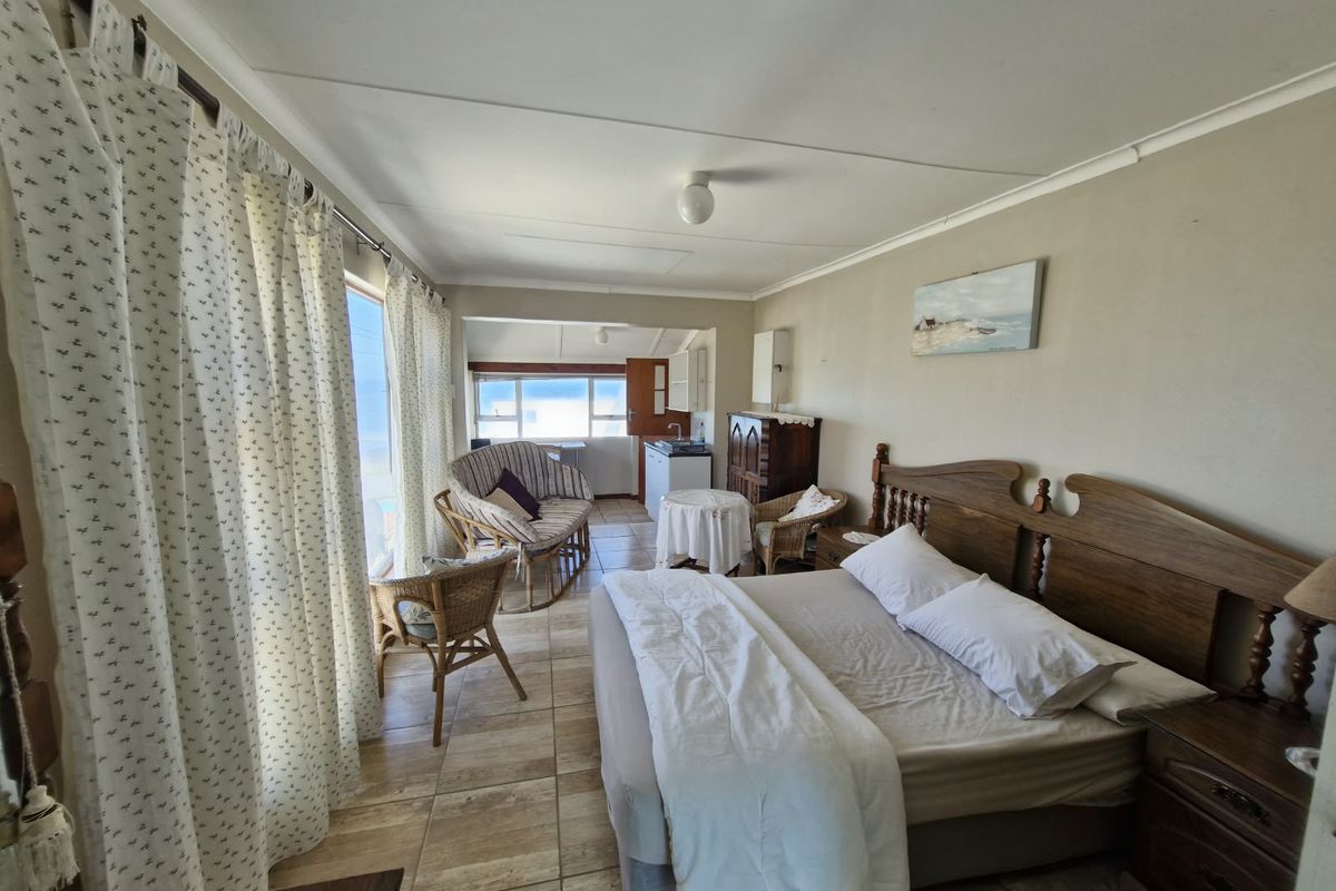 Spacious bedroom featuring tiled flooring, a small kitchenette area, and large windows with natural light, offering a functional and comfortable living space.