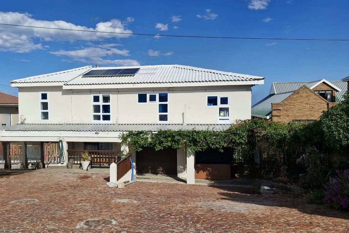 Rear view of a two-story house featuring a corrugated metal roof with solar panels, a brick-paved driveway, and a covered patio area.