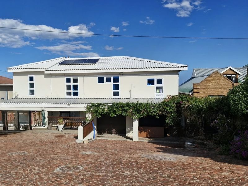 Rear view of a two-story house featuring a corrugated metal roof with solar panels, a brick-paved driveway, and a covered patio area.