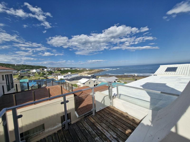 An elevated balcony featuring timber decking and a glass balustrade, offering expansive coastal and neighbourhood views.