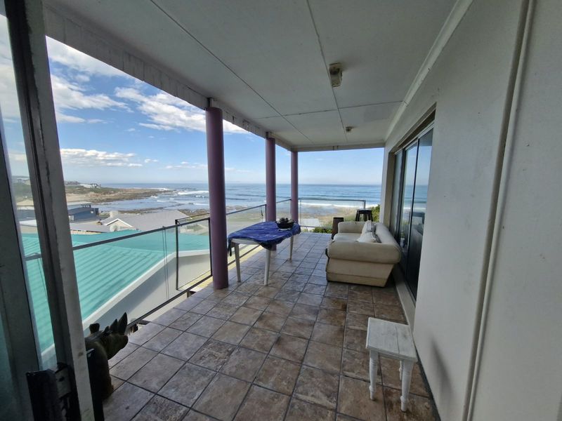 Spacious covered balcony featuring tiled flooring, glass balustrades, and expansive ocean views, providing an ideal outdoor entertainment area.