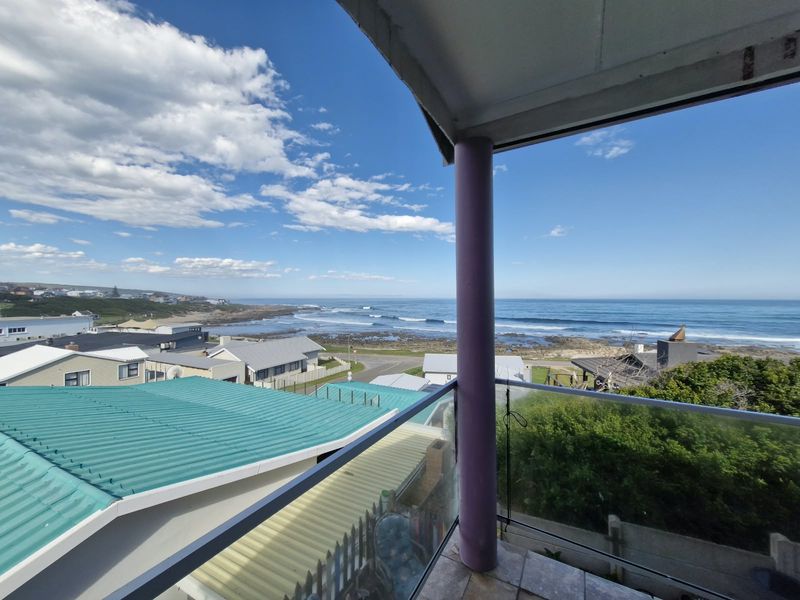 An elevated balcony featuring a glass balustrade and tiled flooring, offering expansive coastal and ocean views.