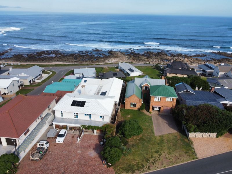 Aerial view of a coastal residential property featuring metal roofing, solar panels, and paved driveway access near the oceanfront.