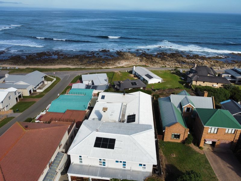 Aerial view of a coastal residential property featuring a white metal roof with integrated solar panels, situated near the ocean.