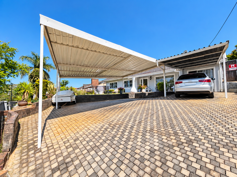 Front exterior view featuring a large paved driveway and dual carport structures providing ample covered parking space.