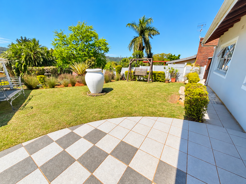 A well-maintained garden featuring a checkered tiled patio, lush lawn, and established landscaping, providing a pleasant outdoor space.