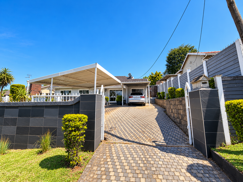 Front view of the property featuring a paved driveway, a modern carport, and well-maintained boundary walls with contemporary tile cladding.