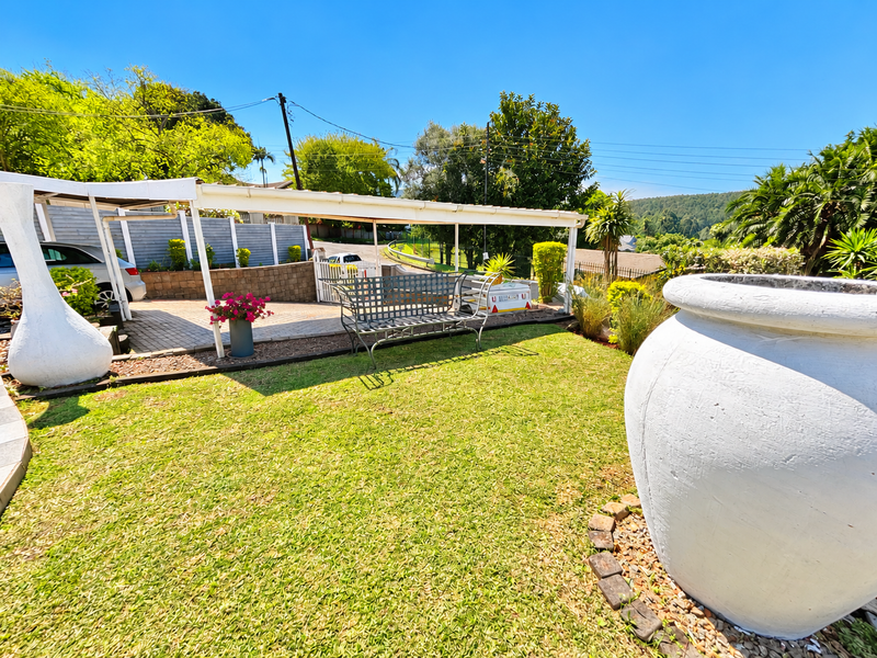 A well-maintained garden area featuring a lawn, paved driveway, and a covered carport structure, providing functional outdoor space and parking.