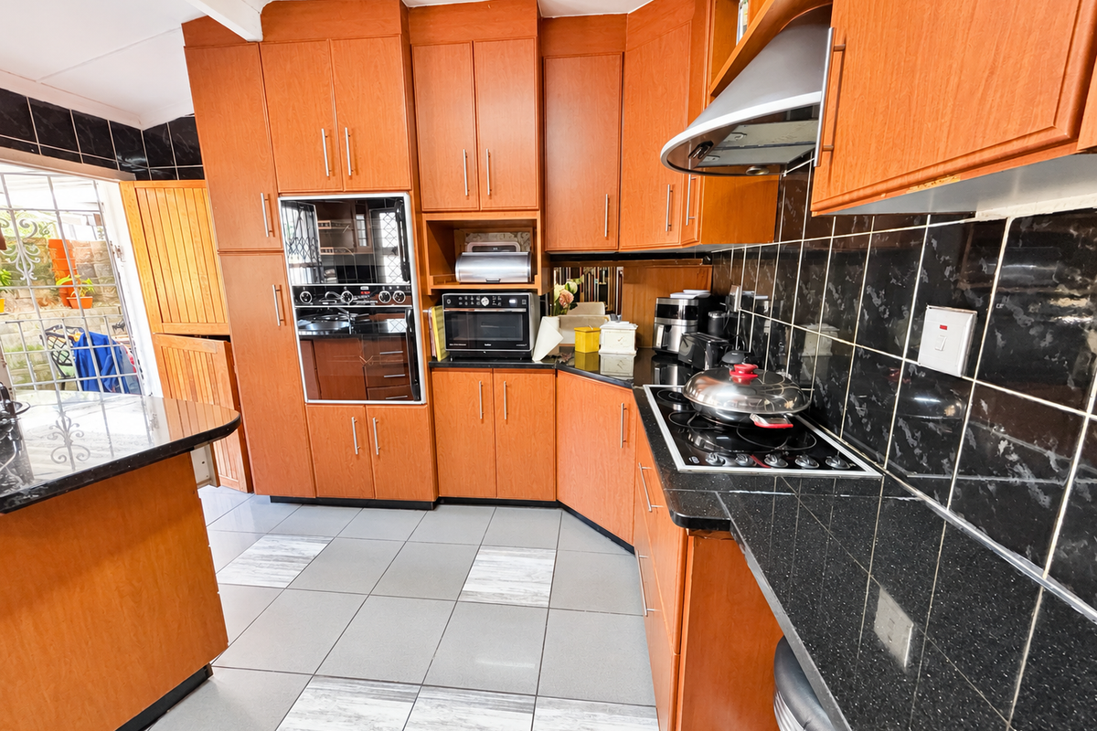 A functional kitchen featuring wooden cabinetry, black granite countertops, a built-in oven, and a hob with an extractor fan, finished with tiled flooring.